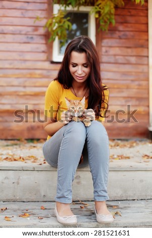 Beautiful young woman sitting on the porch and is holding her cat.