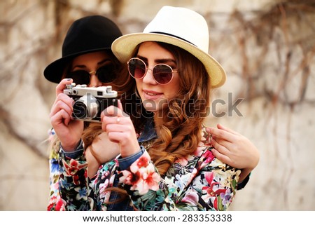 Outdoor lifestyle portrait of two best friends hipsters making photo on their vintage camera having fun together joy and happiness wearing trendy bright clothes and sunglasses Outdoor lifestyle portrait of two best friends hipsters making photo on their vintage camera having fun together joy and happiness wearing trendy bright clothes and sunglasses