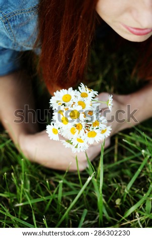 Red-haired girl holding a bouquet of daisies field