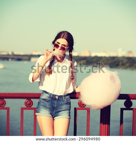 Lifestyle. Young happy hipster woman eating sweetened cotton candy, amazing view of the city from the bridge. Photo toned style Instagram filters.
