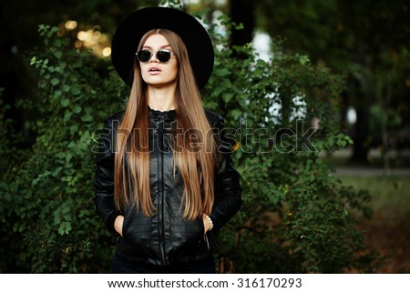 Street fashion concept - pretty young slim woman in rock black style, wearing stylish sunglasses and black leather jacket. Young cheerful fashion woman