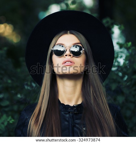 Street fashion concept - closeup portrait of a pretty girl. Wearing hat and leather jacket, round sunglasses. Autumn woman. Artsy bohemian rock style. Fall fashion. Toned style instagram filters