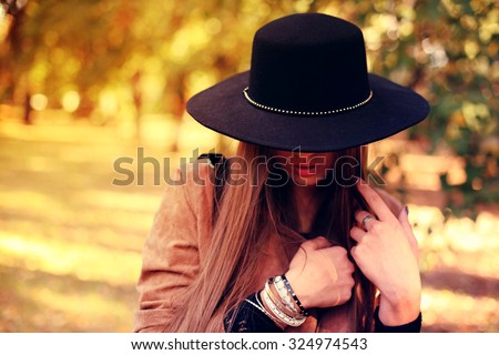 Street fashion concept - closeup portrait of a pretty girl. Wearing hat and suede jacket holding bag with fringe. Beautiful autumn woman. Soft warm vintage color tone. Artsy bohemian style. Outside