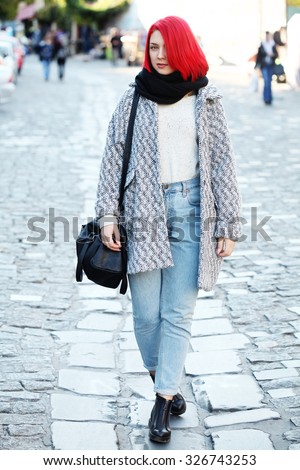 Beautiful red haired woman wearing oversized coat, boyfriend high waisted jeans, black scarf, leather bag and boots, posing outdoors. Street style.