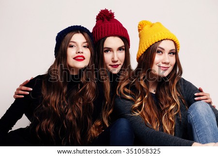 Studio fashion portrait of a group of three young beautiful model posing in winter leather shoes, warm clothes and colorful knitted caps. Friends having fun. Consumer concept, winter fashion