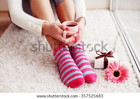 Comfort Concept - Woman drinking hot cocoa. Close-up of female legs in bright colored warm socks with a retro vintage instagram filter.