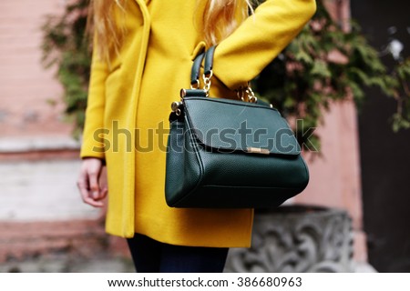 Female fashion concept. Close up. Colorful detail of yellow coat and green leather bag.  Street style