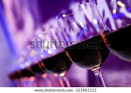 Glasses with red wine lit by nightclub lights on dark-purple background