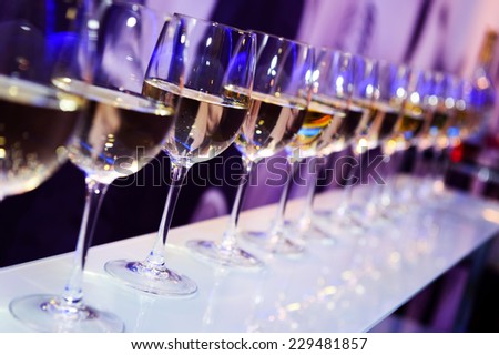 Number of glasses with white wine lit by nightclub lights on dark-purple background