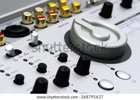 Silver DJ mixer controller with buttons, switches, faders, knobs, other toggle items, plugs and connectors, selective focus