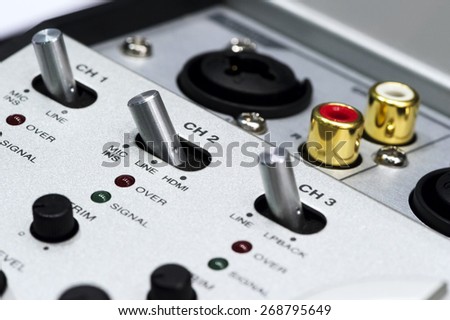 Detail of silver DJ mixer controller with buttons, switches, faders, knobs, other toggle items, plugs and connectors, selective focus