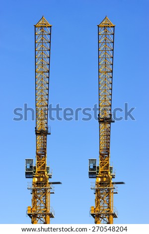 Construction yellow cranes towers isolated on blue sky background, two synchronously parallel standing objects