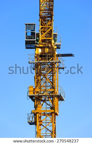Construction yellow crane tower with operator cabin isolated on blue sky background, detail