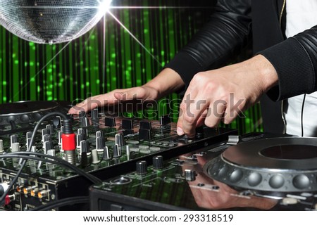 DJ at dance party mixes track on sound mixer, nightclub with striped green interior and silver disco ball with star, professional stereo electronic equipment