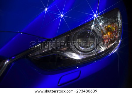 Fragment of the hood and headlights sports blue car with silver stars