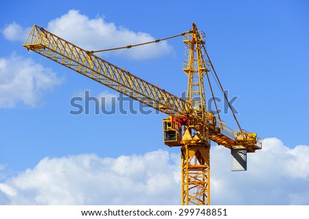 Yellow construction tower crane isolated on blue sky with white clouds background