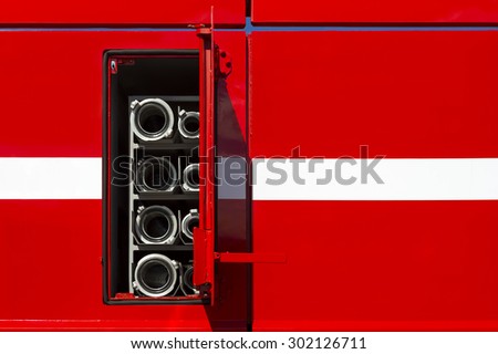 Firefighter car body with fire hoses and pump in compartment with open door, red bodywork with white line of emergency vehicle, rescue service
