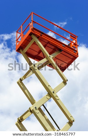 Scissor lift platform with hydraulic system at maximum height range painted in orange and beige colors, large construction machine, heavy industry, white clouds and blue sky on background