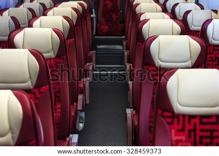 Bus seats in row with red leather and textile coating, wooden armrests, white headrests and mounts for safety belts, modern comfortable tourist transport interior, selective focus