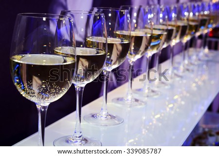 Nightclub wine glasses with white wine lit by party festive lights on dark-purple background, nightlife