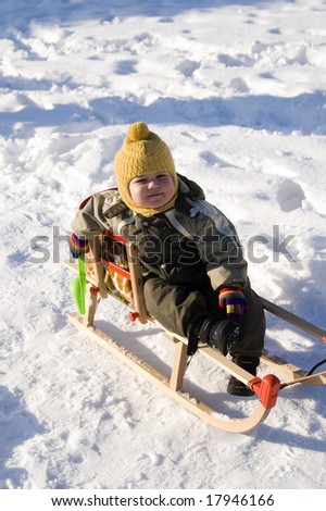 Baby in green coat sitting in sled sled in snow-covered park