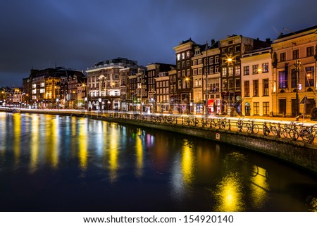 AMSTERDAM, THE NETHERLANDS - AUGUST 7: Traditional Dutch houses aligned  along a canal on August 7, 2013 in Amsterdam, The Netherlands. A tram in motion left a light trail on Rokin Avenue.