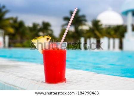 Glass of Strawberry Daiquiri cocktail standing on the swimming pool ledge in an tropical resort