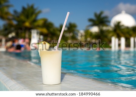 Glass of pinacolada cocktail standing on the swimming pool ledge in an tropical resort