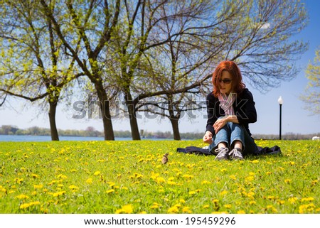 Woman sits in a yellow dandelion field and talks to a sparrow on a sunny morning
