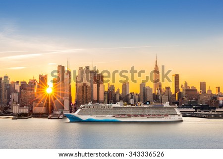New York City skyline at sunrise, as viewed from Weehawken, along the 42nd street canyon. A large cruise ship sails Hudson river, while sun beams burst between the skyscrapers.