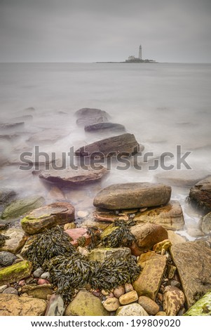 The waves slowly glide over exposed rocks and seaweed infront of St. Mary\'s Lighthouse
