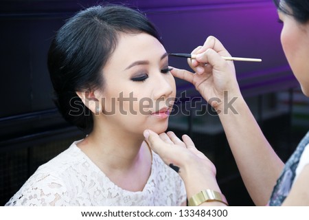 Make-up artist applying cosmetics on a beautiful young asian lady