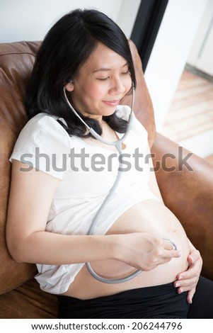 Pregnant woman using stethoscope to listen to the heartbeat