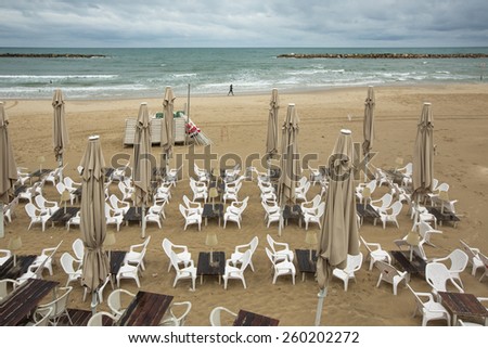 Empty tables and chairs in the beach near sea, on a rainy day