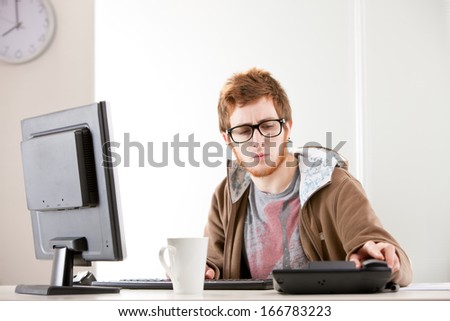 A young redheaded clerk is looking perplexed at his black desk telephone