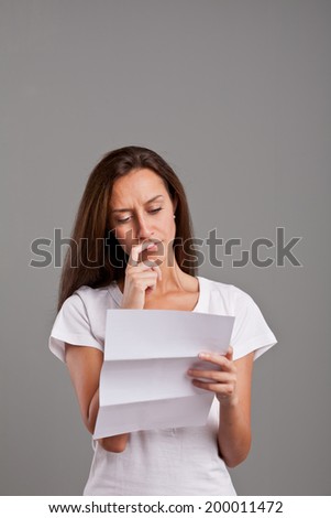 brunette girl reading uncertain news on a white document on a neutral gray faded background