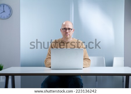 office worker with a nerd attitude and an open laptop on the top of an empty desktop in an almost empty room waiting for you to act