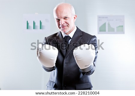 smiling self confident businessman challenging the observer with a pair of boxing gloves
