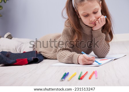 little girl on the floor colouring on her notebook using felt-tip pens
