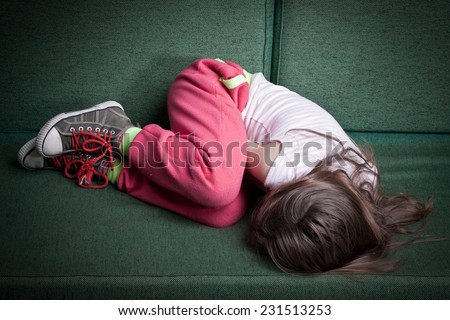 little girl curled up in fetal position on a couch protecting herself from danger or cold