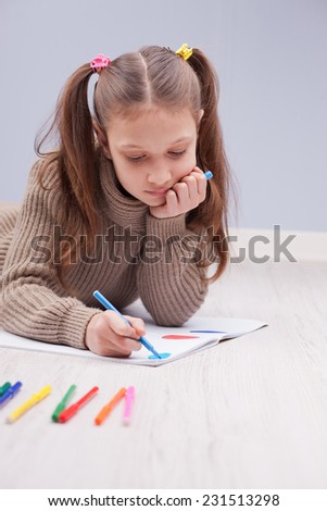 little girl on the floor colouring on her notebook using felt-tip pens