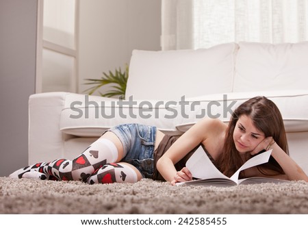 pretty girl reading a book on her rug in front of her sofa in her living room