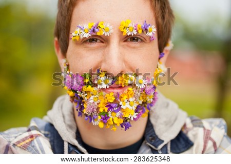 young hipster man with his beard and eyebrows covered with flowers looking at camera with a sly smile but very self confident