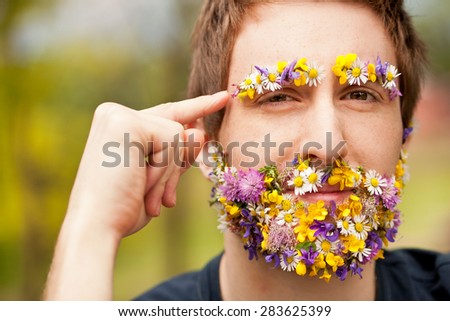 young hipster man face-covered with flowers makes an hand gesture meaning he wants you to think about environment and green power
