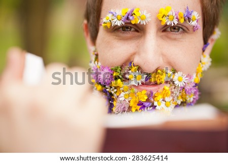 full nature immersion for this hipster young man reading a book having his face covered with flowers instead of his beard and eyebrows