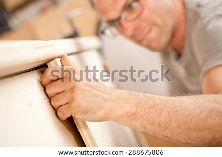 focus on the robust hand of a carpenter holding a flap (a wooden board) he\'s placing on a piece of a handcrafted wooden piece of furniture