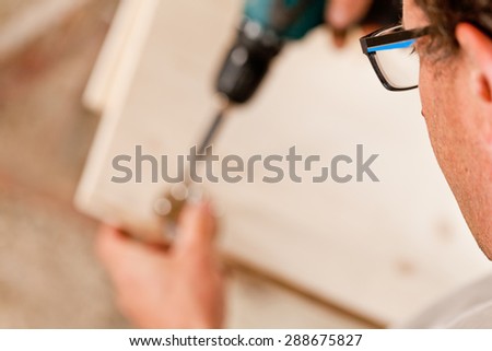 shallow depth of field with focus on the glasses of the carpenter using a drill driver on a component of a piece of furniture