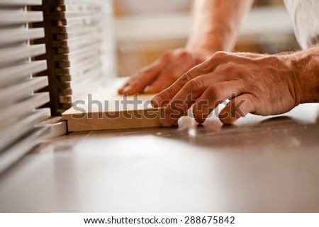 robust hands of a man working on a wood shaper (spindle moulder) in a carpenter workshop, detail of a board being shaped