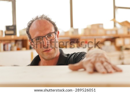 carpenter in his joiner\'s workshop laying his hand on the wooden surface of a piece of furniture