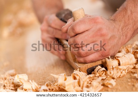 closeup of woodworker\'s hands shaving with a plane in a joinery workshop